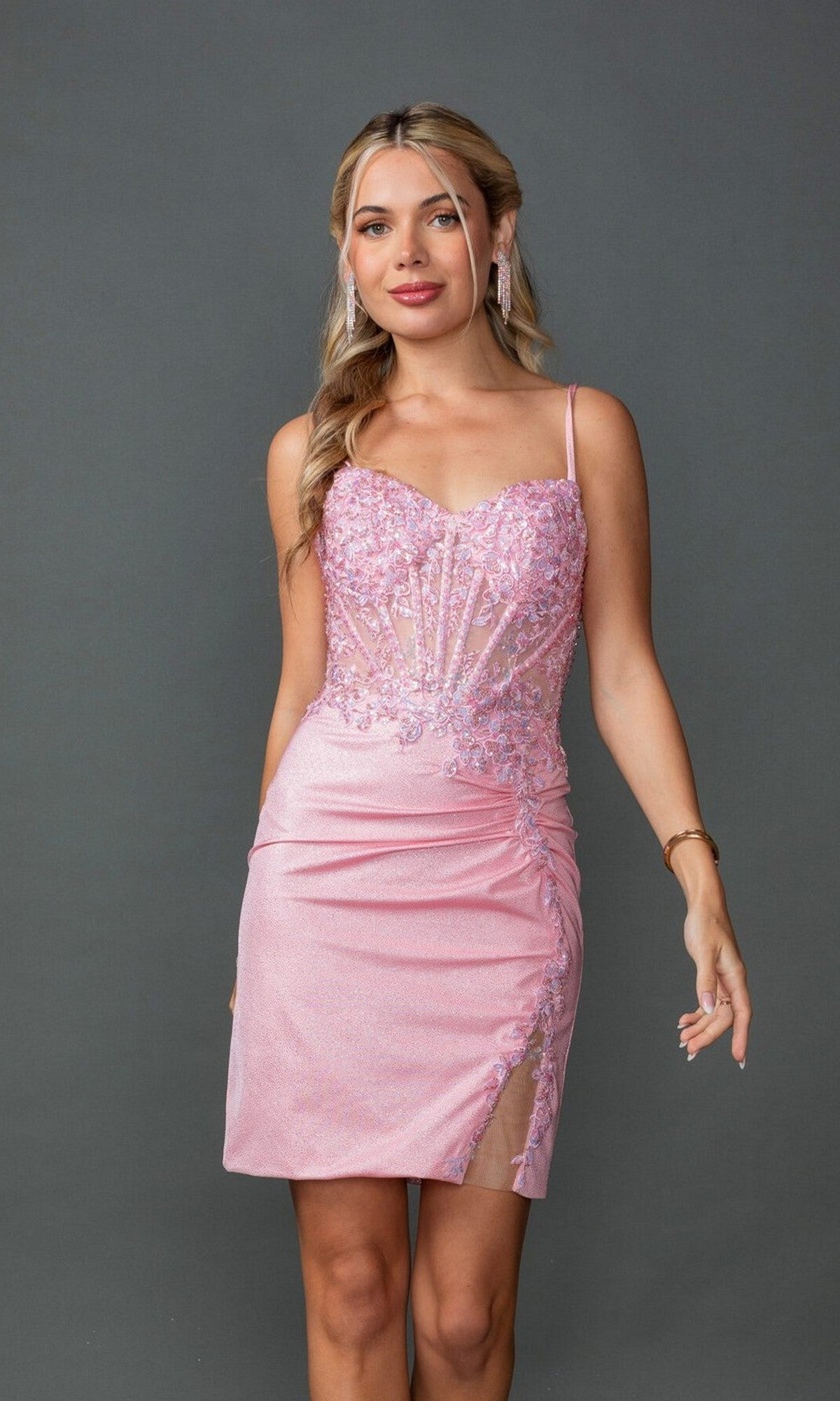 A woman stands against a gray background wearing the Dancing Queen 3427 short prom dress, featuring a light pink fitted silhouette with lace details and a sheer overlay.